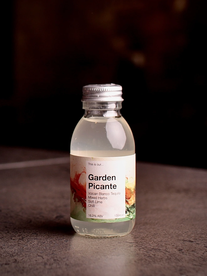 A mini bottle of Garden Picante shot against a moody dark background 