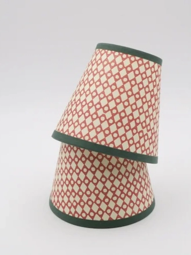 Candle Clip Shades. Two small candle lampshades in a coral and cream diamond lattice print with dark green trims, stacked on a plain white background. The hand-printed shades are ideal for chandeliers, wall sconces and candlestick lamps.