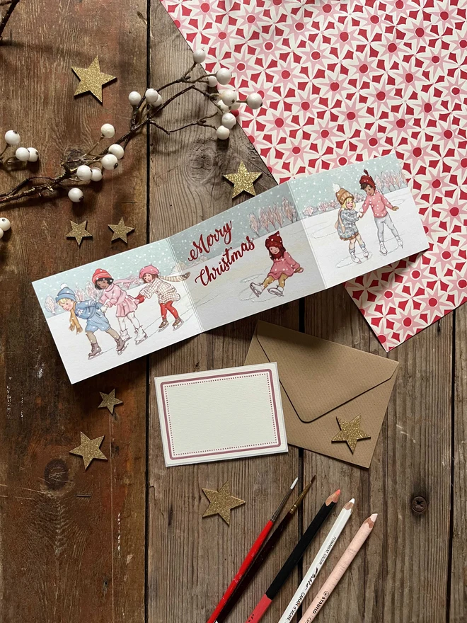 a Christmas concertina style retro vintage Christmas Card featuring illustrations of children ice skating with snow and hand finished with glitter says the words Merry Christmas comes witha kraft envelope and vintage style address label