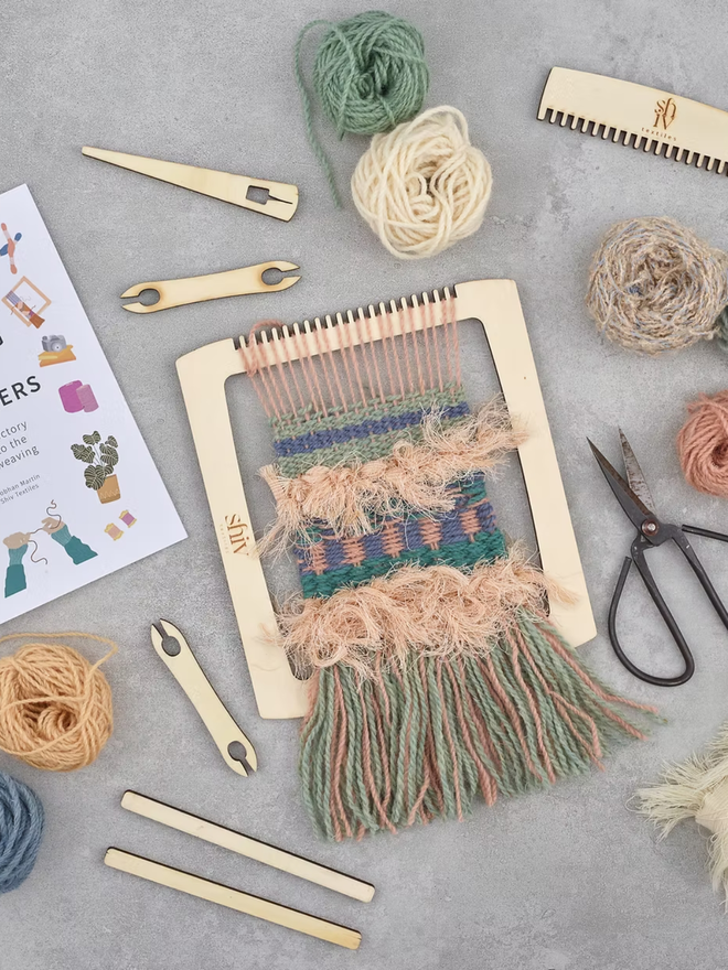 beginners' weaving kit. a wooden weaving kit and colourful yarn displayed on a white backdrop.
