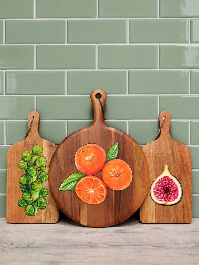 A collection of wooden serving boards with handpainted designs, standing on a kitchen counter