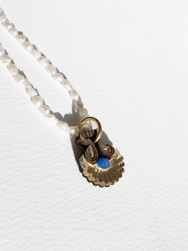 Pearl necklace with a shell shaped gold pendant & gemstone on a white background