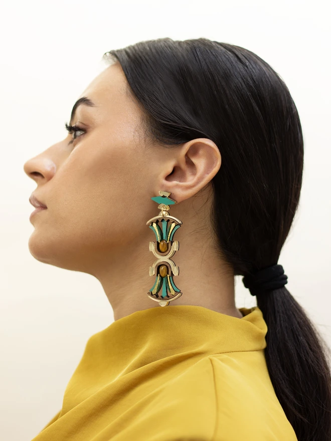 A person wearing a gold and green earring with a blurred background