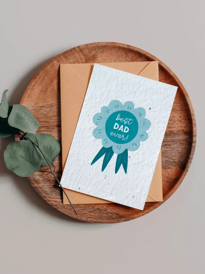 Illustration of a blue rosette with ‘Best Dad Ever’ on it on a wooden tray next to a Eucalyptus branch
