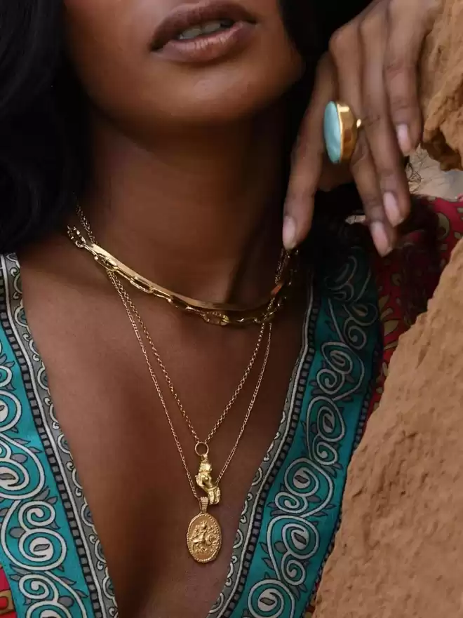 Model wearing gold goddess pendant with longer gold oval pendant featuring Hindu goddess Durga with gold chains on model