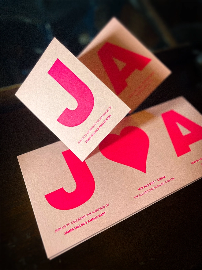Close-up of luxury Amour concertina wedding invitation featuring oversized personalised initials and heart, letterpress printed in fluorescent hot pink on Candy Pink card.