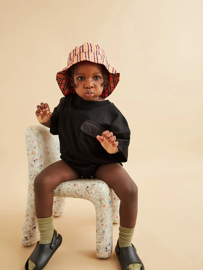 cool toddler wearing oversized baby romper in black sat on a kids ecobirdy chair. Romper is by www.studiokoter.com and stocked in ando stores cissy wears word store and triangle uk childrens stores