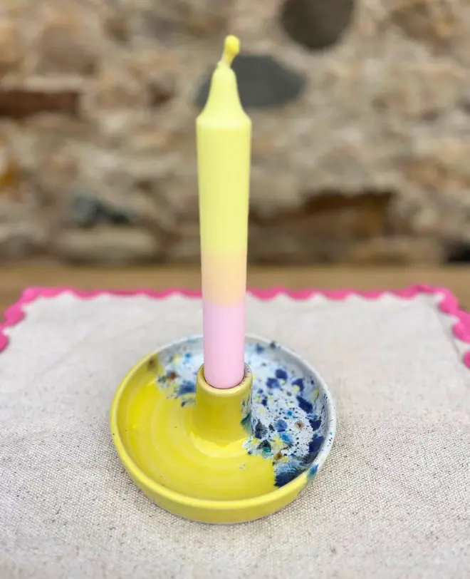 Shoreline Candle Stick Holder, a colourful candle stick holder sitting on a napkin, on a wooden surface against a brick backdrop. 