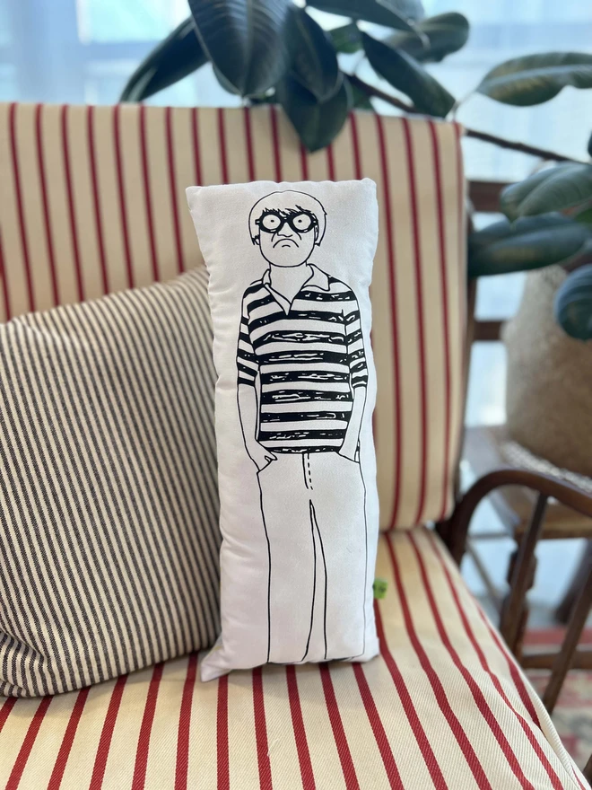 Black and white illustrated screen printed cushion of British artist David Hockney. The cushion sits on a striped sofa.
