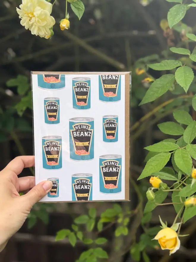  baked beans tins illustrated card. card photographed against rosebush backdrop.