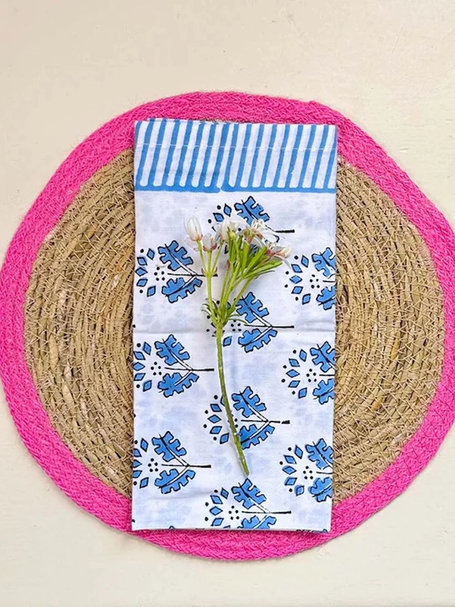 Close up of a seagrass placemats with pink rings, shown on a light surface with flower napkin placed on top. 