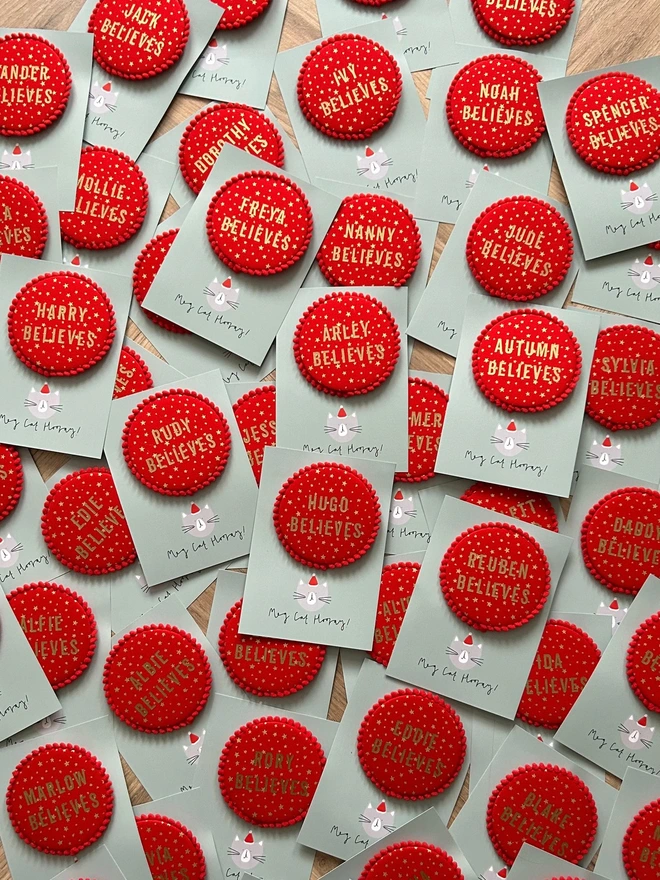 Red christmas 'Believe' badges with gold stars and a red pom pom trim and a child's name 
