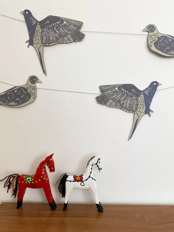 Paper garland hanging over white wall with wooden horses below 