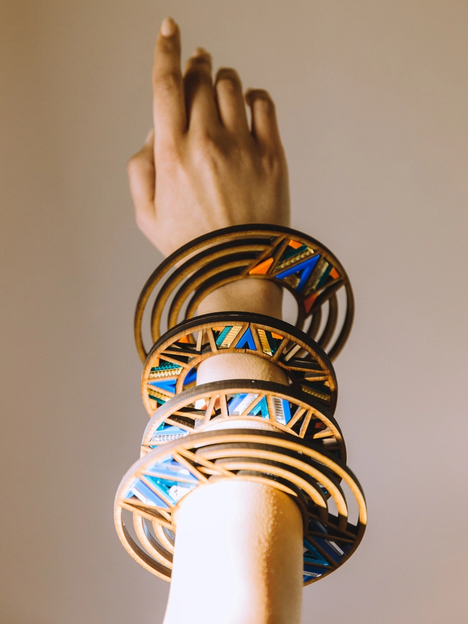 A hand modelling intricate patterns bangles made mostly from walnut wood. Some of the bangle has multi ringed.