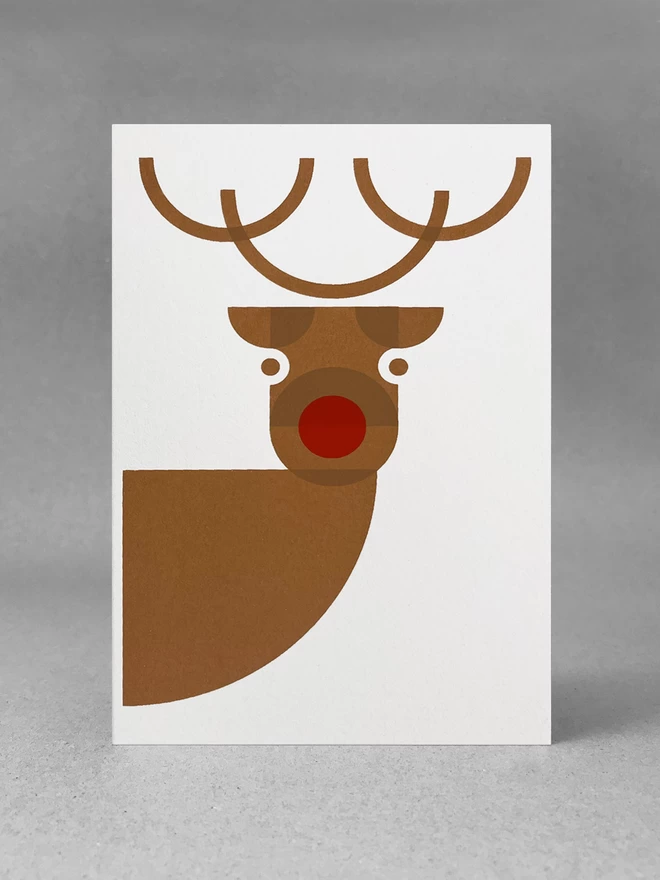 Flat on front view of a Cheeky reindeer handprinted christmas card, looking right at you. Stood in a studio setting. Screenprinted in browns and red.