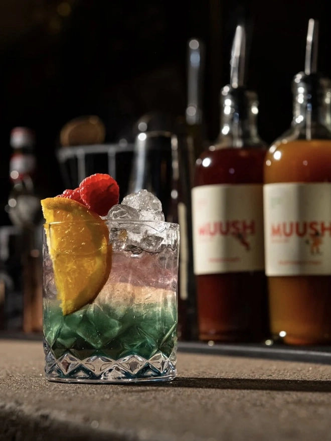 Raspberry & Lychee Elixir, a soft drink sat on a stone surface accompanied by other bar equipment. 