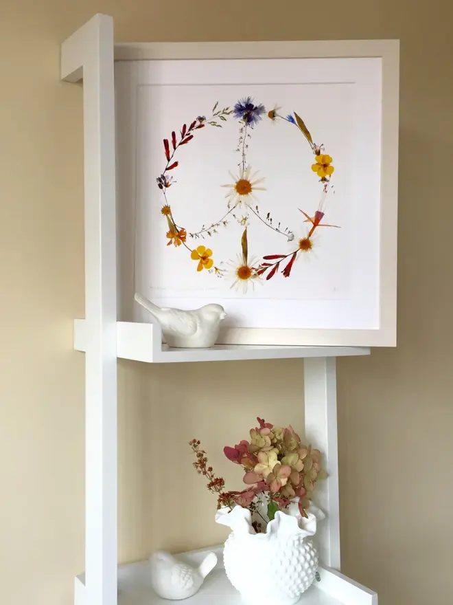 Pressed Wildflower Peace Sign Print, a wildflower peace sign print sitting framed against a stand. 