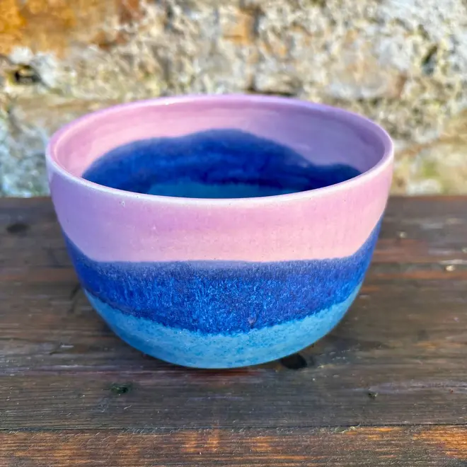 Landscape Small Bowl, a colourful bowl sitting on a wooden surface against a brick backdrop. 