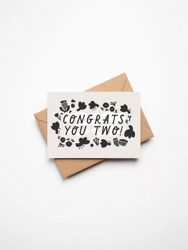 Black and white greeting card with illustration and the words congrats you two written on it with a brown envelope underneath it. 