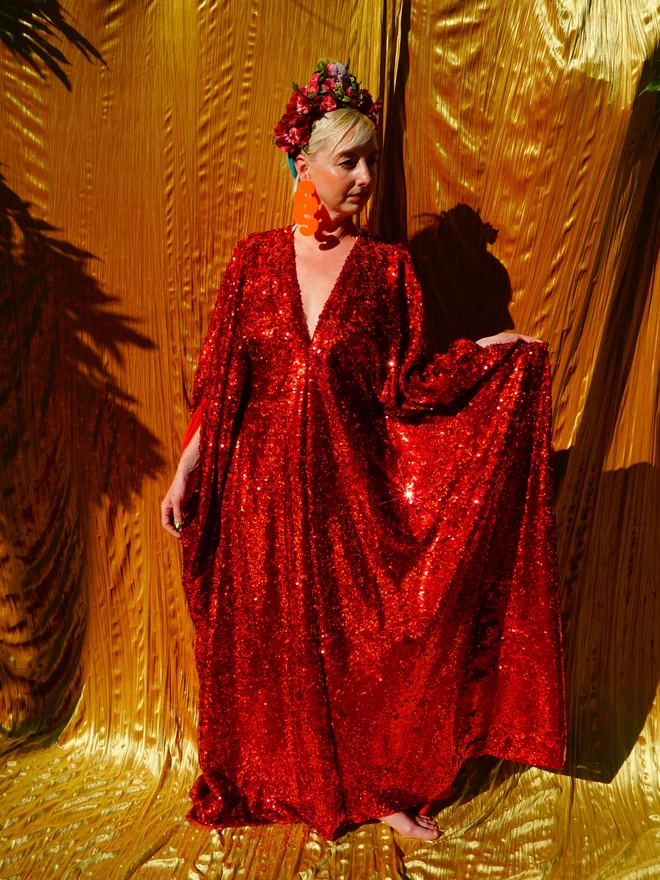 Red Holographic Sequin V-neck Kaftan Gown seen worn by a woman lifting her skirt up.
