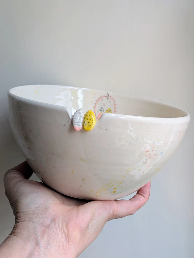 budgie couple bowl held aloft with the back of a pink and yellow bird watching themselves in a hand painted mirror opposite with splatters of colourful glaze