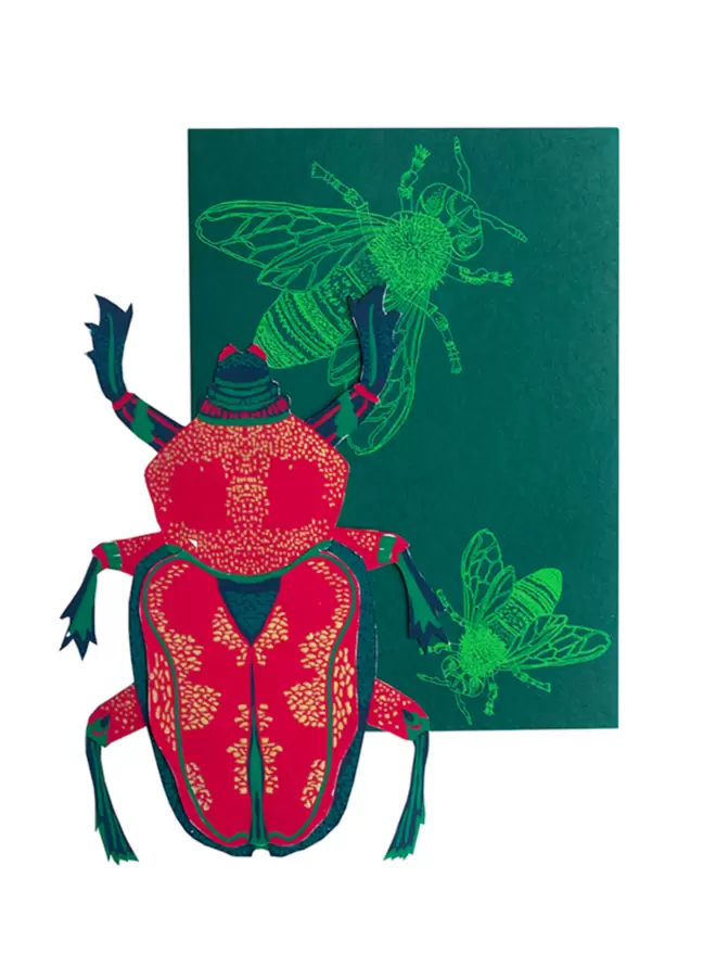 White cut-out shot: red and gold beetle with matching green envelope that shows insect motif 