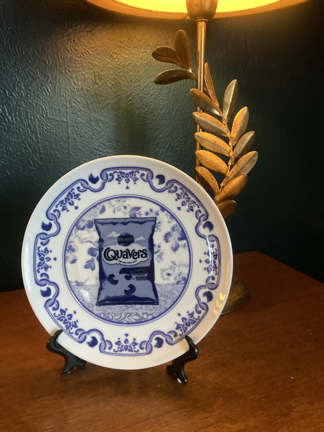 Blue and white Delft style decorative plate featuring a packet of Quavers crisps in the centre.