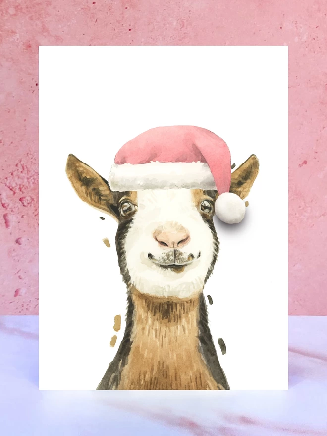 A Christmas card featuring a hand painted design of a goat, stood upright on a marble surface. 