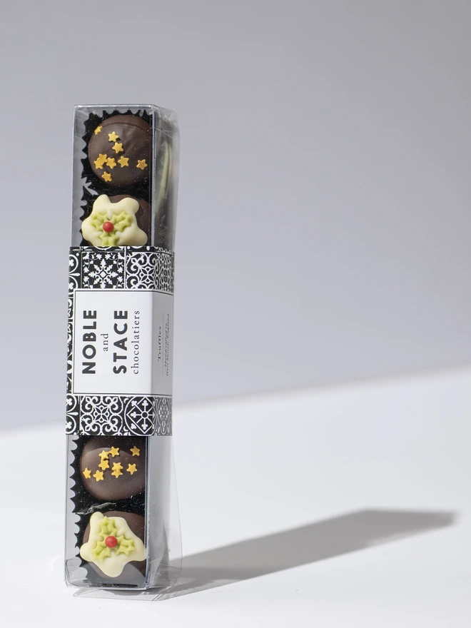 A tube of 6 dark chocolate Christmas truffles, 3 decorated with edible stars and 3 decorated with white chocolate and a holly leaf.