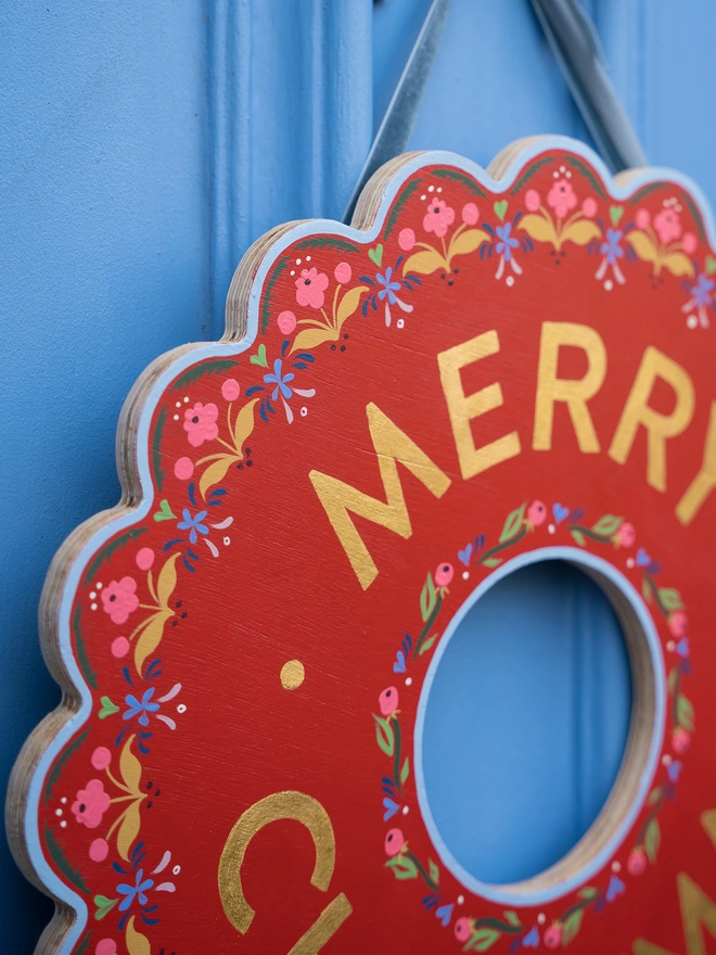 Red Hand painted Christmas Wreath with red lettering and gold leaf lettering on a blue front door