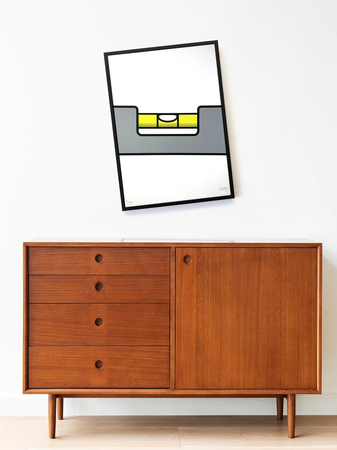 Spirit Level screen print, hangs wonky in a black frame, but the image is level. Hung above a mile century modern sideboard in warm wood tones. All set in a plain interior.