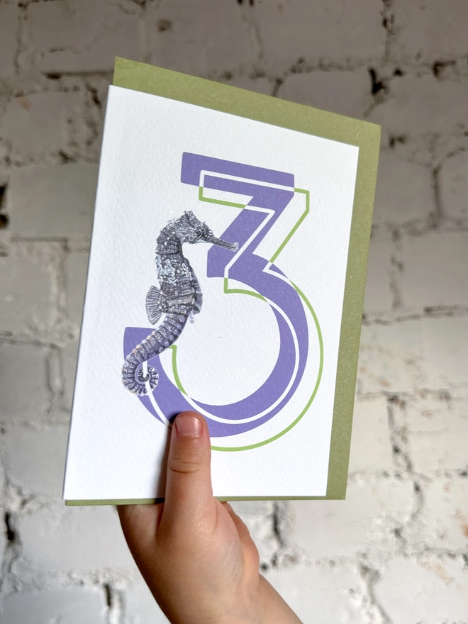 a white card with a big purple number 3 and an illustrated seahorse with a green envelope