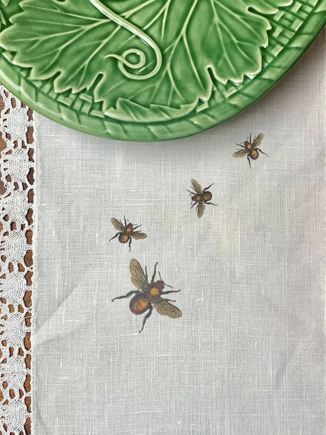 A linen and lace table runner with hand printed bees and a green majolica platter