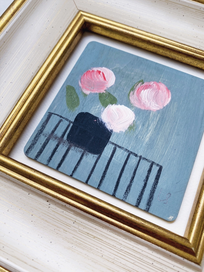 close up of picture of three painterly pink flowers on dusty blue background in a cream and gold 1960's style frame