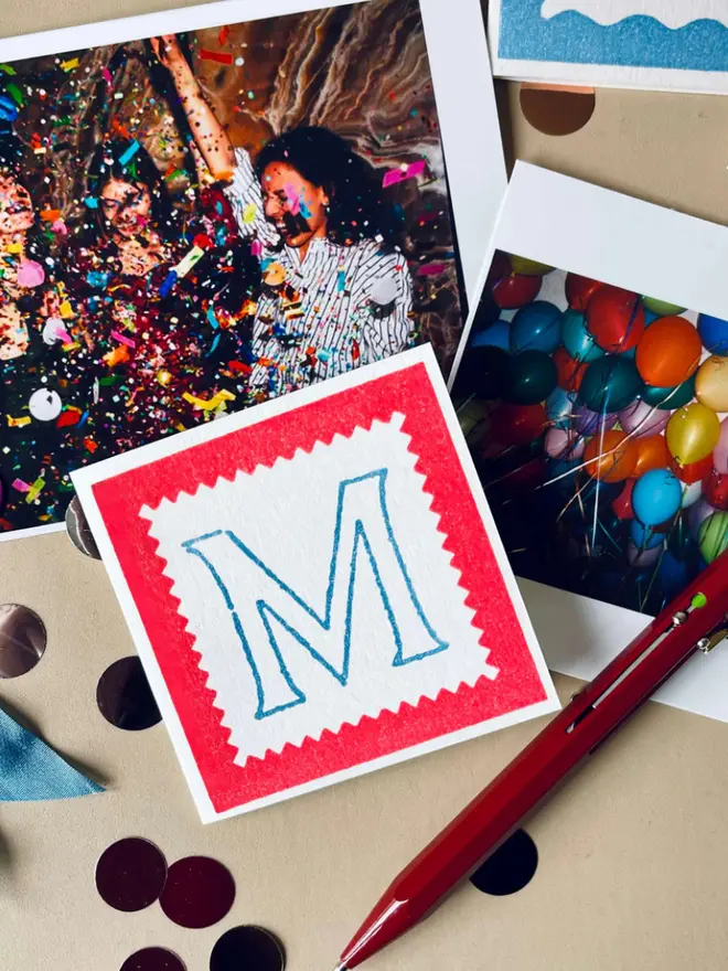 Hand-printed mini letter cards featuring an blue  “M” on a red background, framed with scalloped edges.