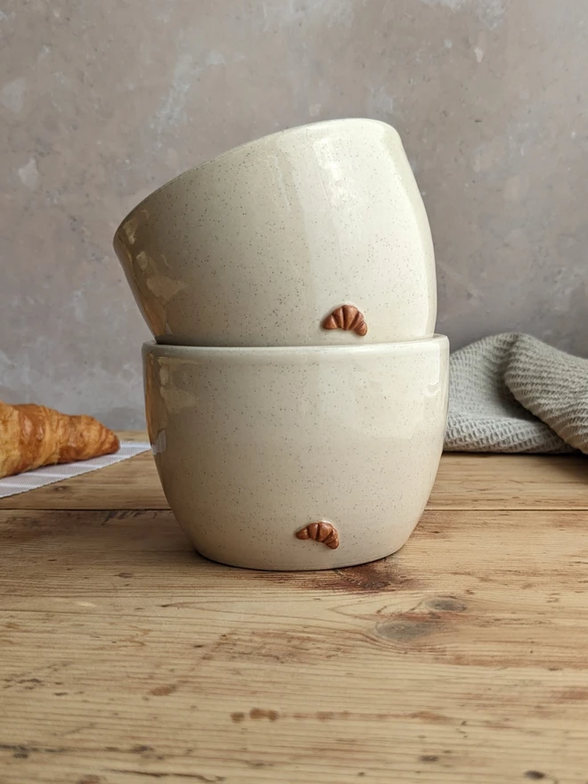 Two croissant coffee cups in vanilla bean glaze stacked together on a grey background.