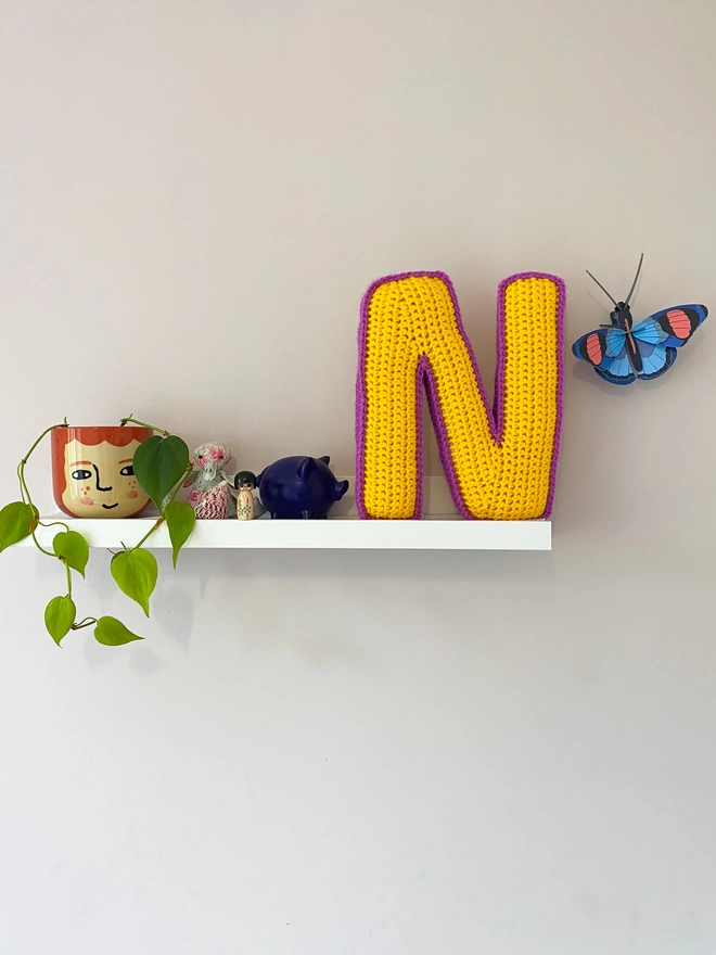 Crocheted N Cushion in Sunshine Yellow & Magenta, on child's shelf