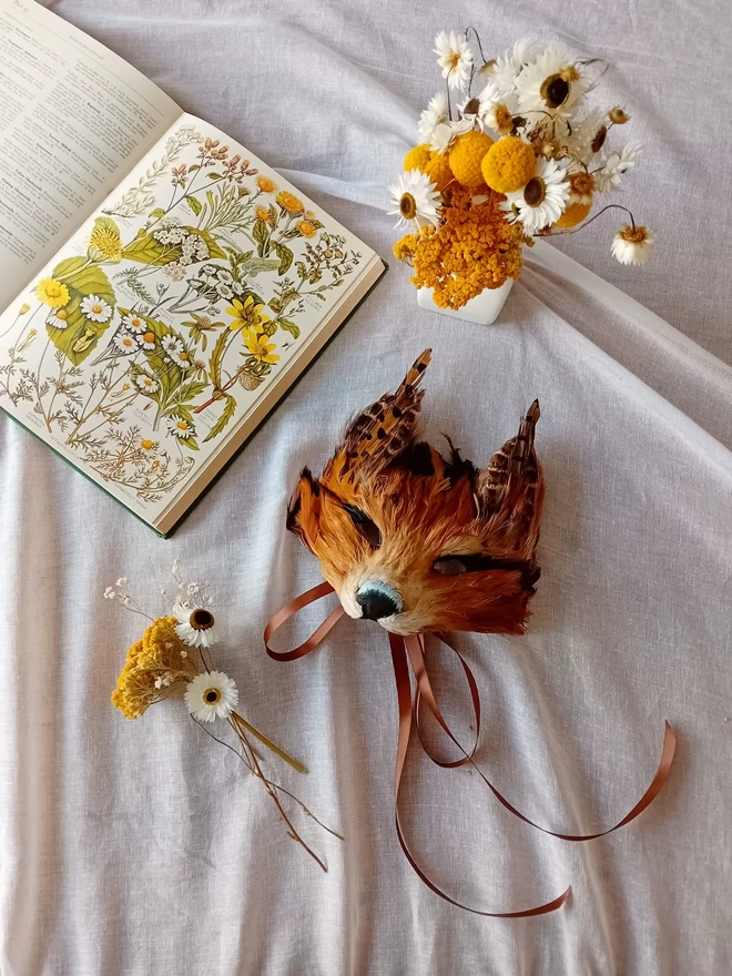 A kid's luxury red fox mask flat lay with yellow and white flowers and a botanical book