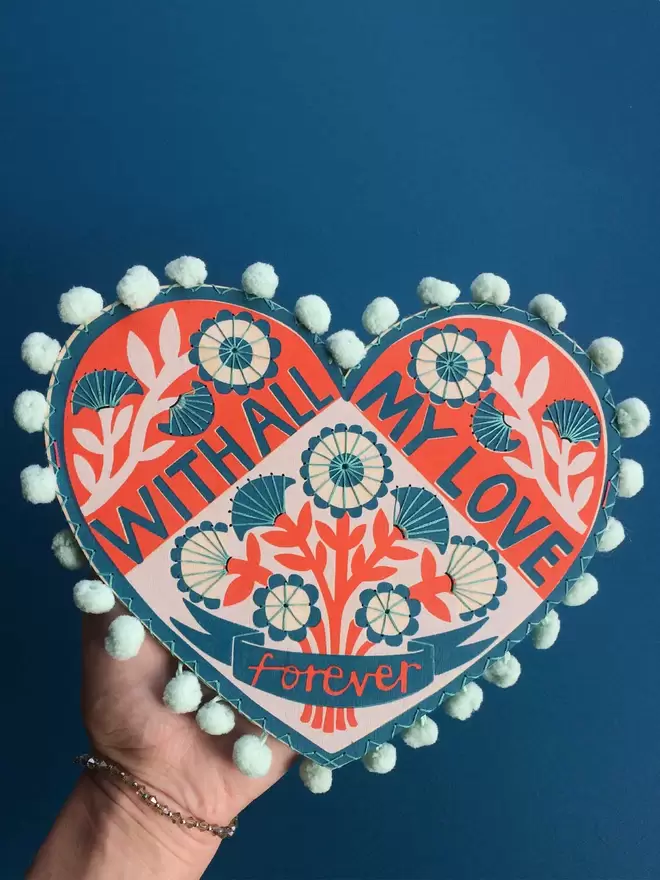 Fiona's hand holds a colourful wooden valentine heart which reads 'With all my love, forever’