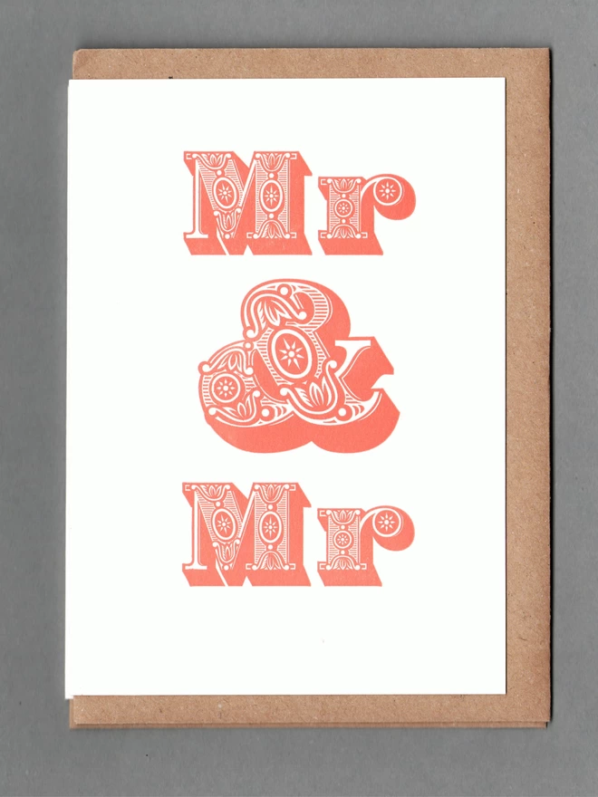 White card with orange text reading 'Mr & Mr' with a kraft envelope behind it