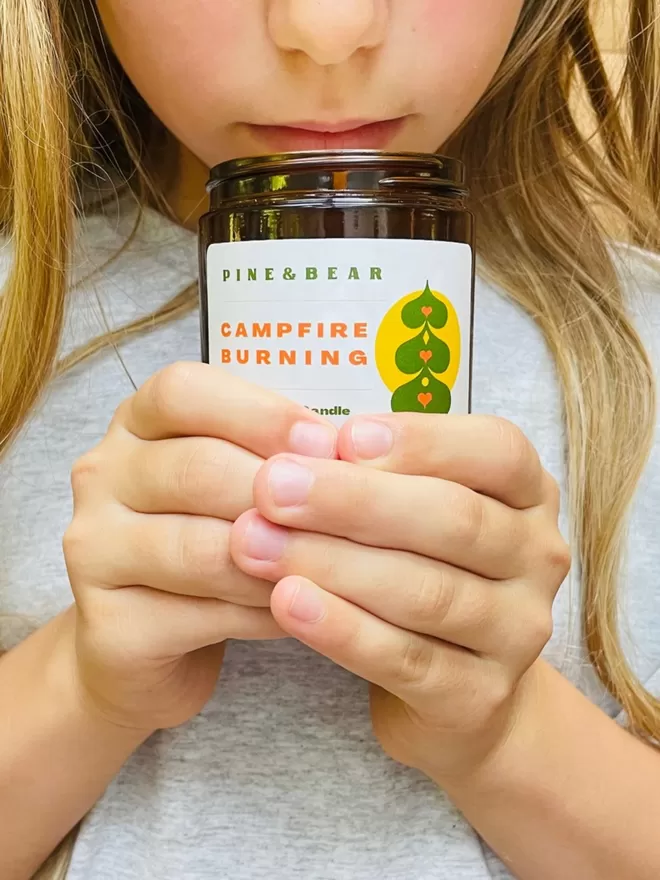 A girl holding a campfire burning natural wax candle.