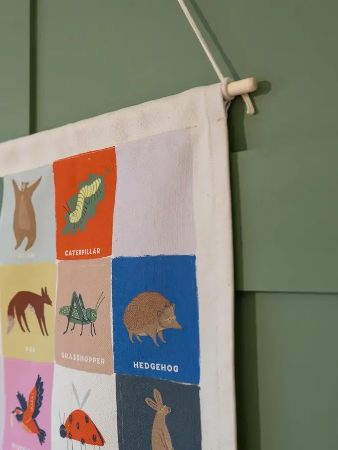 Rainbow Woodland Alphabet Fabric Banner, hanging in a green wall. 