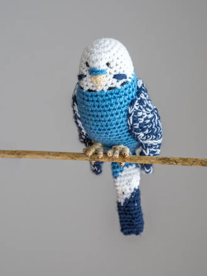 Budgerigar Hand Crocheted Figure, a blue  crocheted bird sitting on a wooden poll. 