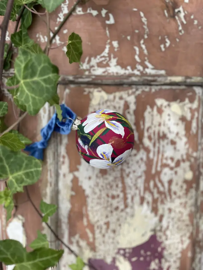 Hand painted floral ceramic christmas bauble dark pink background with Algerian winter iris flowers.