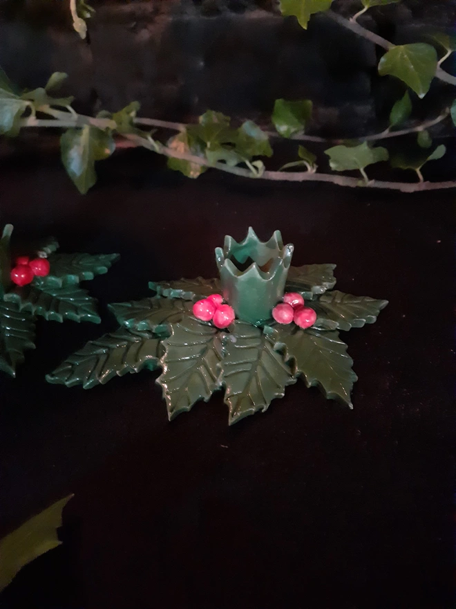 Glossy green holly candle holder with veined leaves and red berry clusters surrounding an empty central candle cup.
