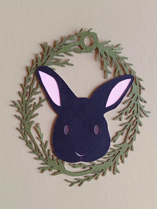 Black Bunny Easter Tree Decoration. Black bunny face with brown eyes and pale pink ears inside olive green foliage wreath oval