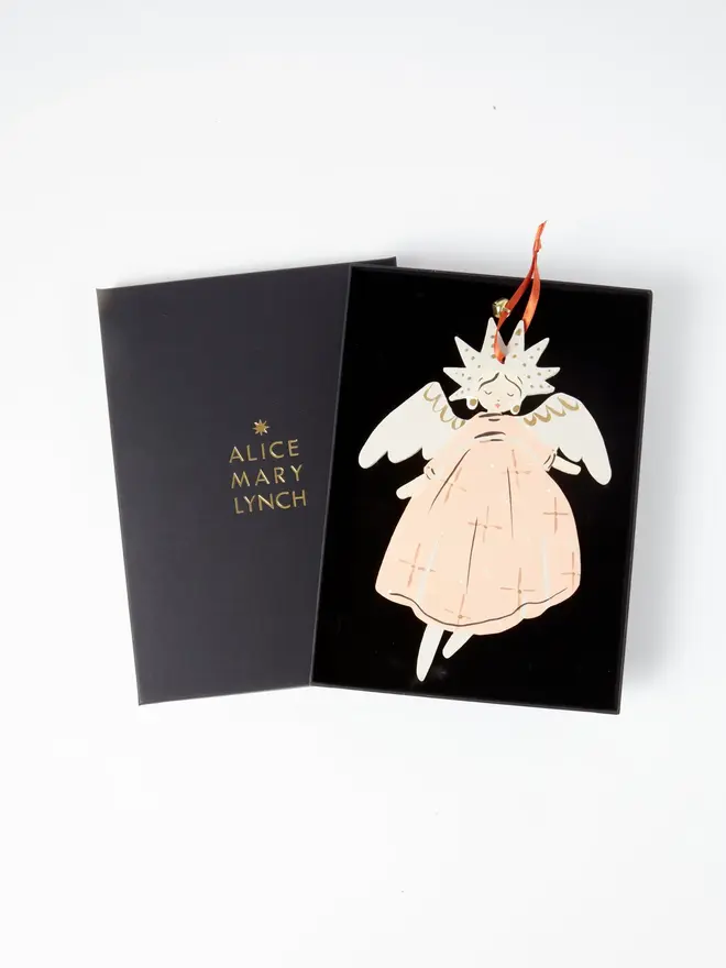 Angel Tree Dancer. wooden hanging angel decoration in an open black gift box embossed "alice mary lynch" in gold, with a star-shaped gold-flecked halo, cream wings and peach star-patterned gown, orange ribbon with a jingle bell