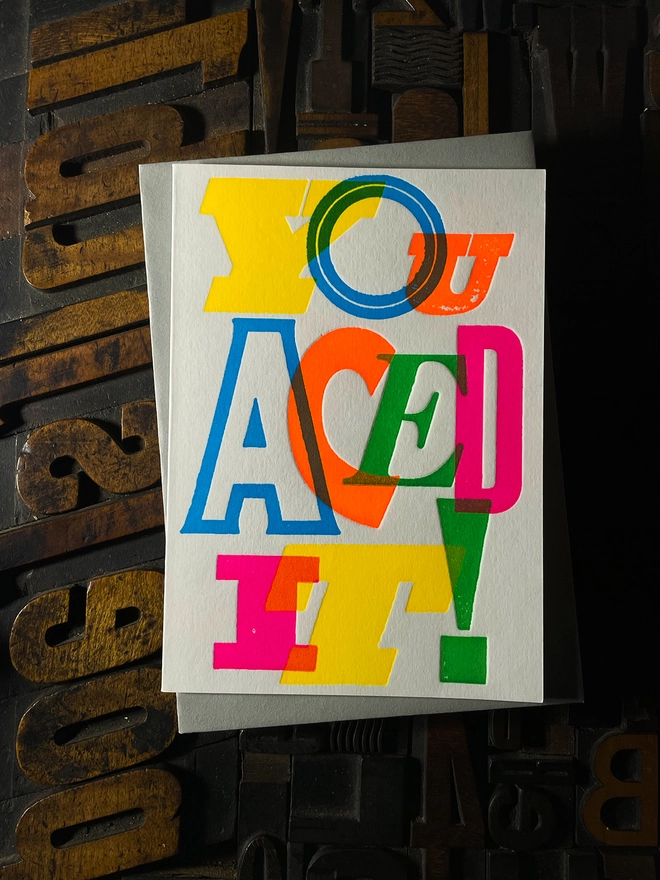 Colourful typographic letterpress card with bold overlapping neon letters spelling ‘You Aced It!’, perfect for celebrating exam success.