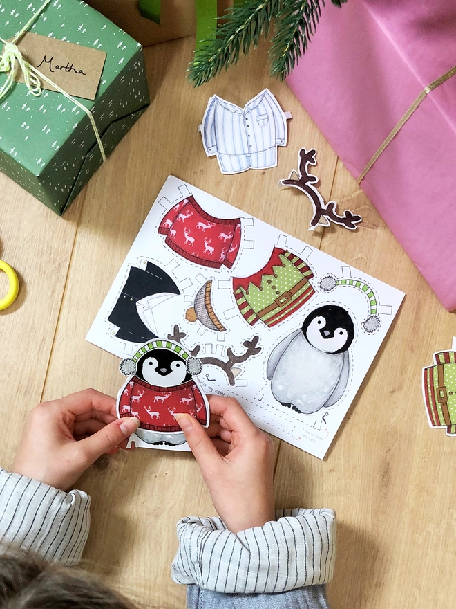 A child is playing with a dress up penguin paper doll that has been cut from a Christmas greetings card.