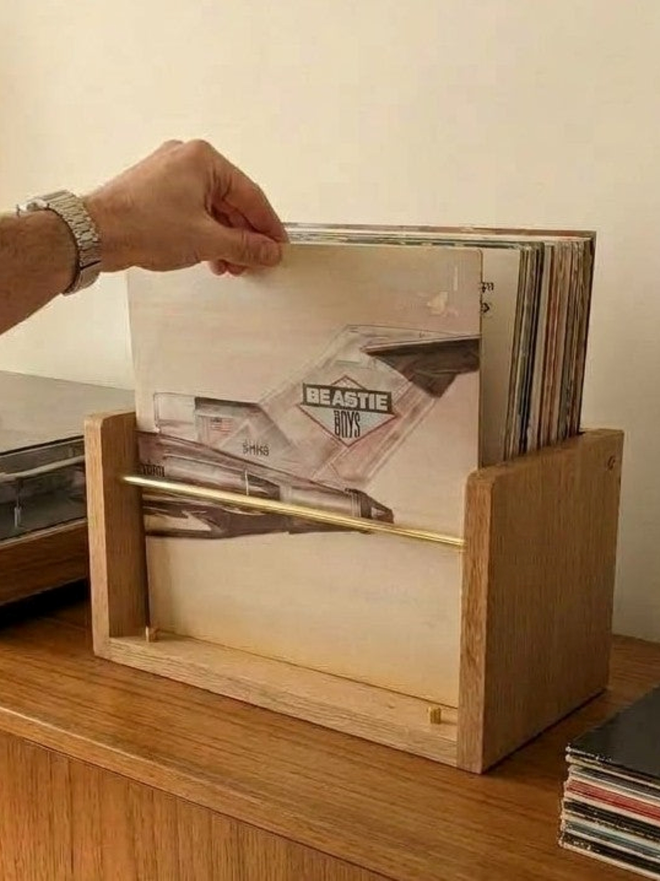 Hand flipping through vinyl LPs in a solid oak record browser with a brass front rail